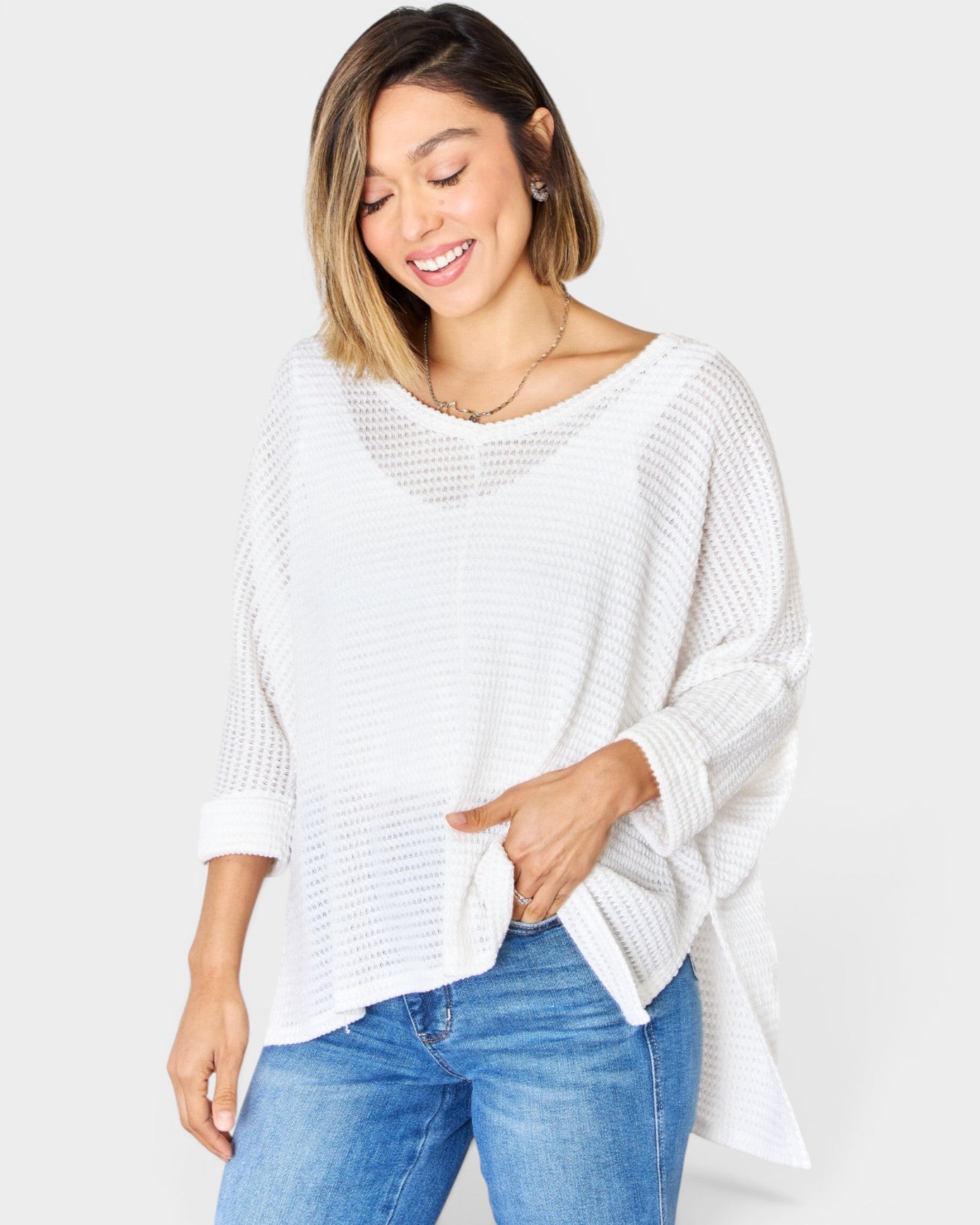 Woman wearing a white sweater and blue jeans on a light gray background