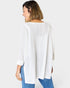 Woman wearing a white textured sweater and blue jeans on a white background