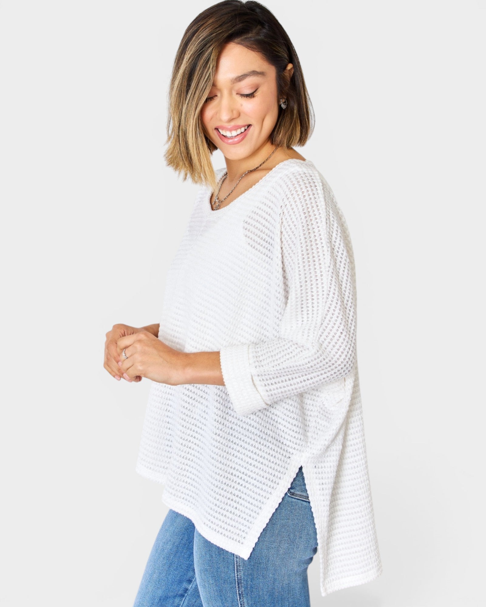 Woman wearing a white knit sweater and blue jeans on a plain background