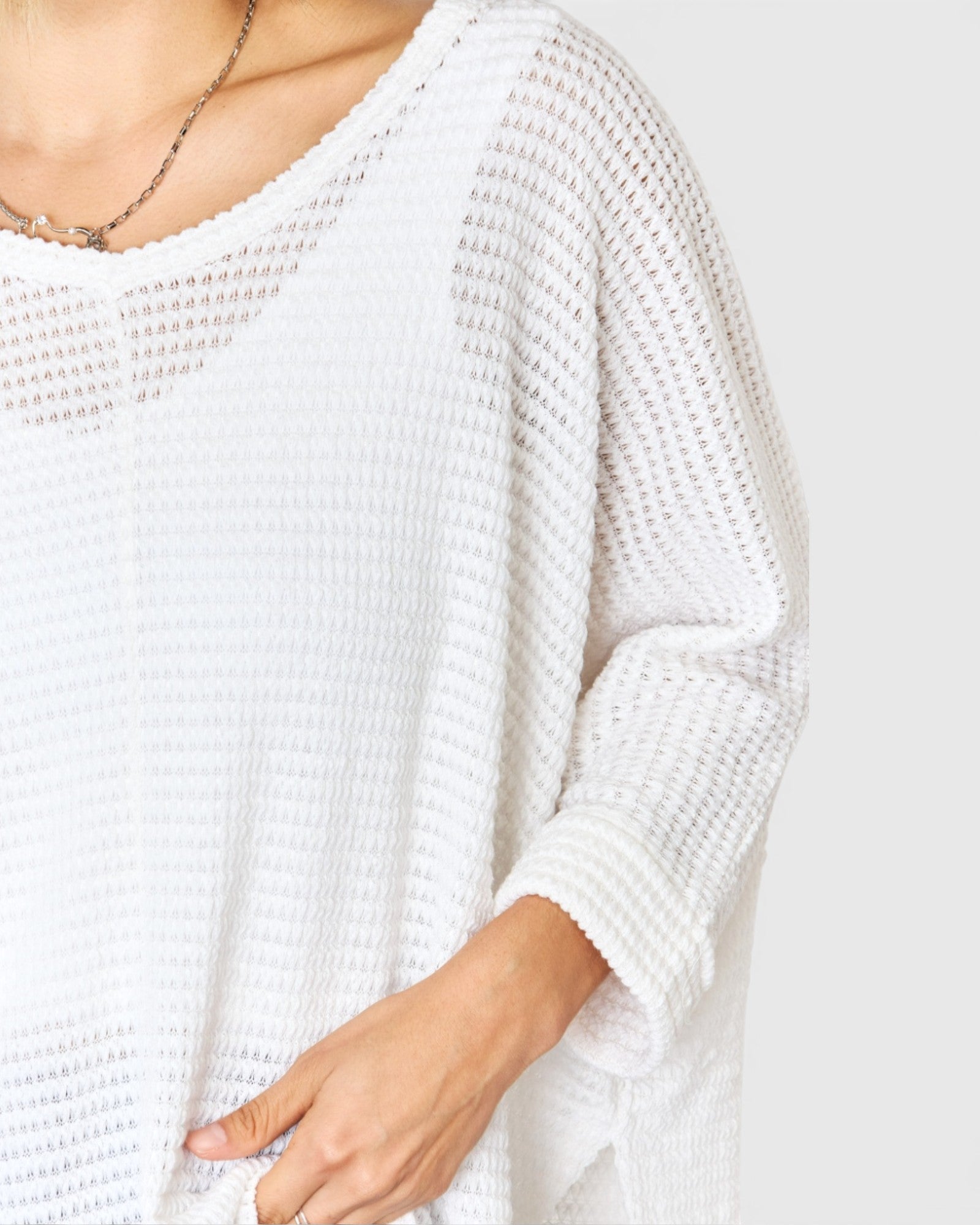 White textured sweater worn by a person on a plain background