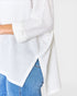White knitted poncho draped over a person wearing blue jeans on a white background