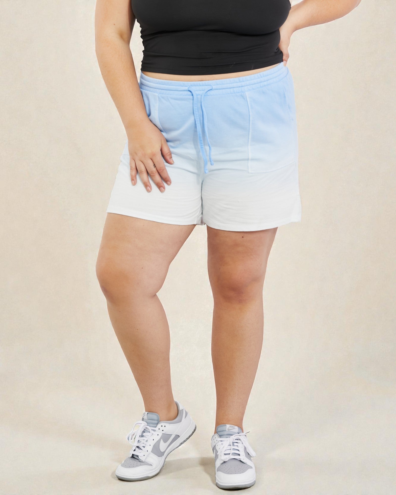Person wearing a black top and blue and white gradient shorts on a beige background