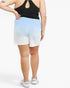 A person shown from the back wearing light blue-to-white gradient athletic shorts, a black sports bra, and white sneakers against a plain light gray studio background.