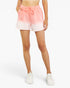 A model wearing a pair of pastel tie-dye shorts with a pink-to-white gradient, featuring a drawstring waist and side pockets, paired with white sneakers against a plain white background.