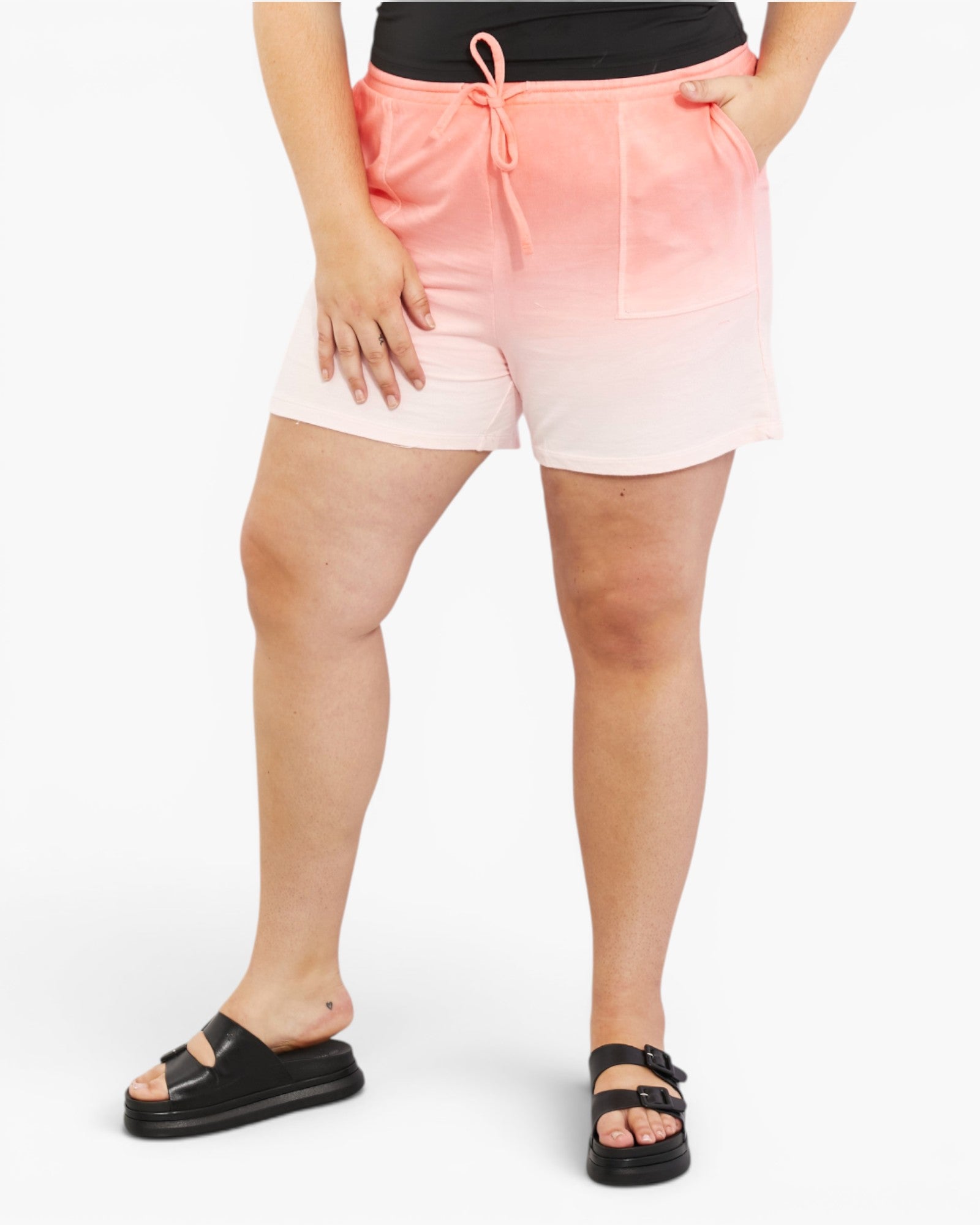 A model wearing a pair of pink and white gradient drawstring shorts, styled with a black top and black slide sandals against a plain white background.
