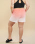 Person wearing a black sports bra and pink to white gradient shorts on a beige background