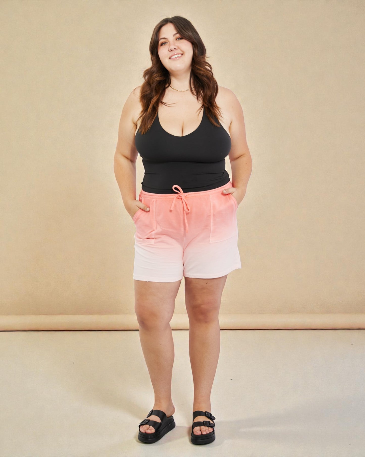 Woman wearing a black tank top and gradient shorts on a beige background