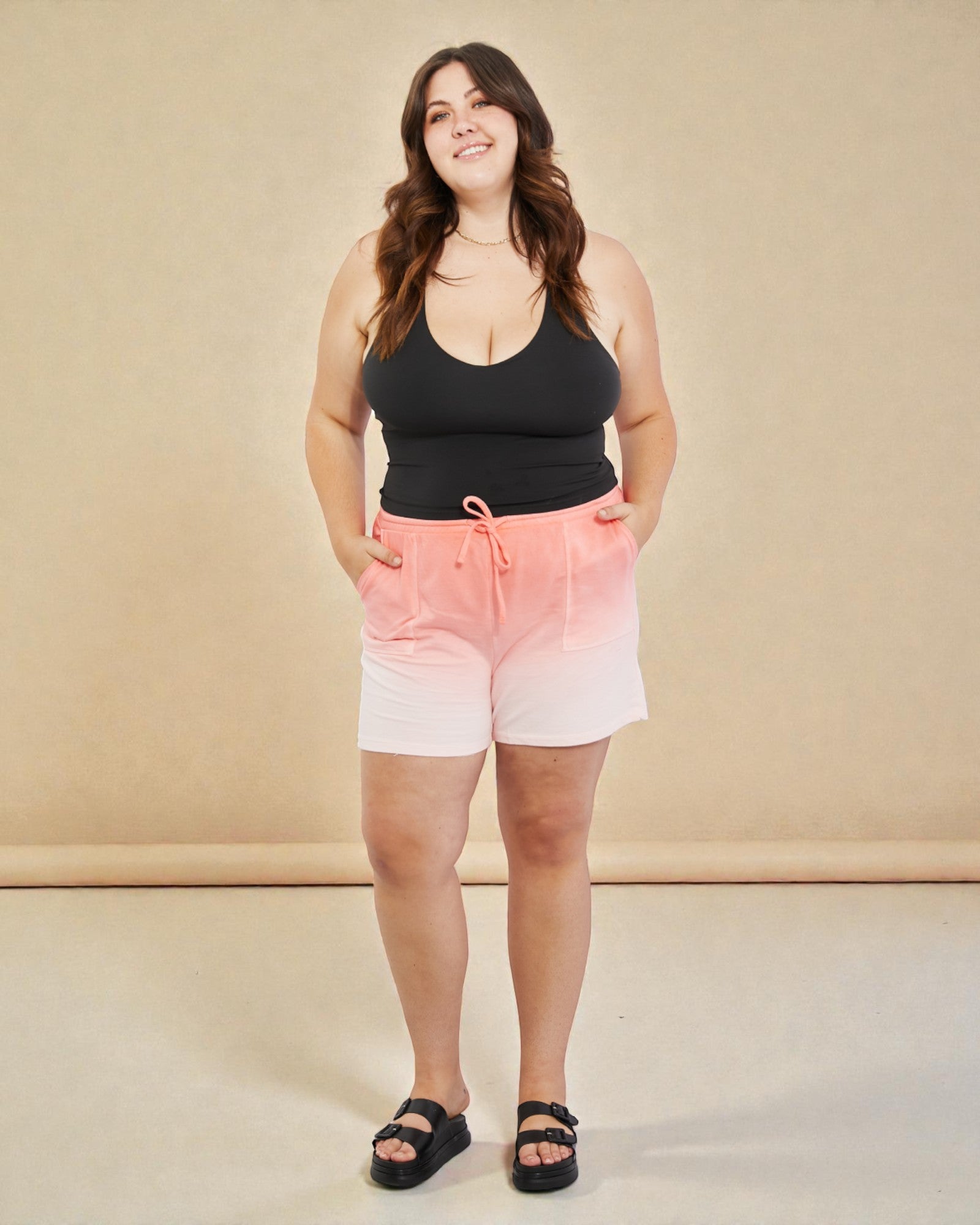 Woman wearing a black tank top and gradient shorts on a beige background