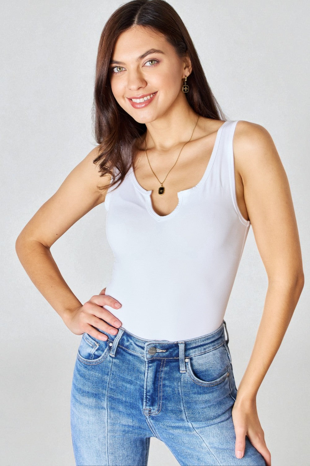 Woman wearing a white tank top and blue jeans against a plain background