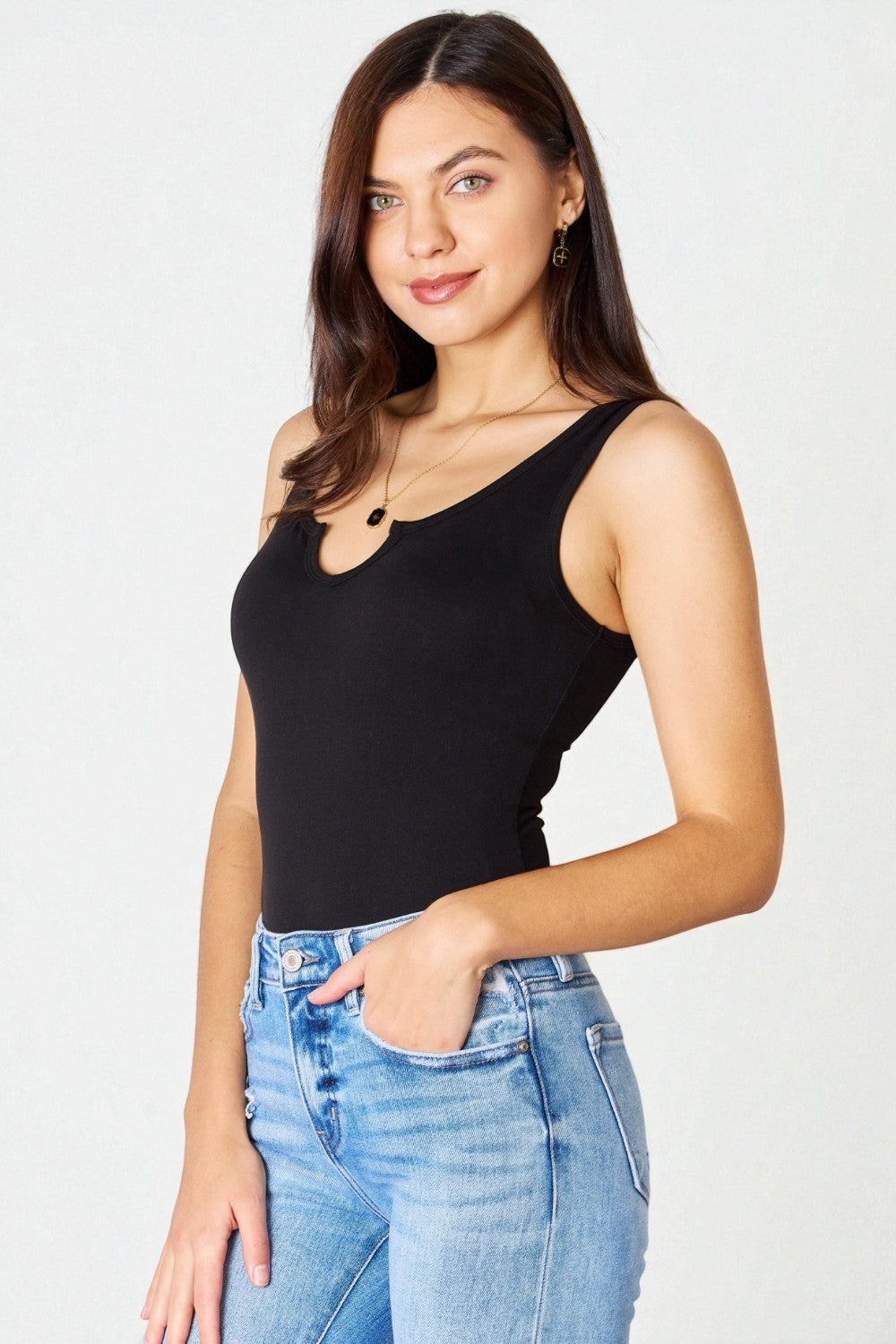 Woman wearing a black tank top and blue jeans against a white background