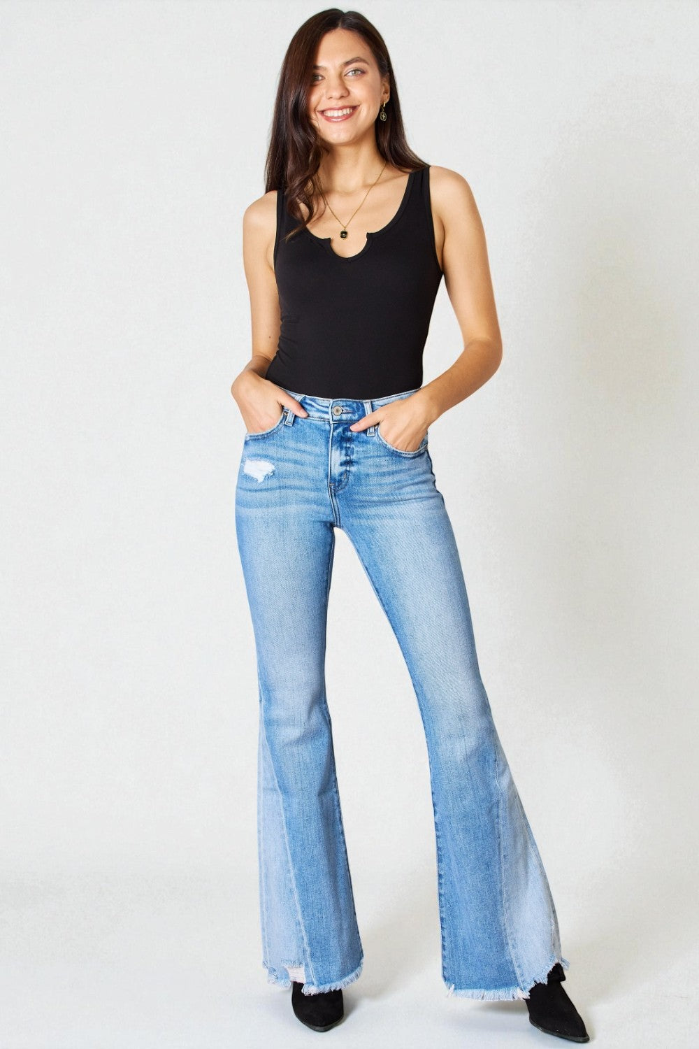 Woman wearing light blue flared jeans and a black top on a white background