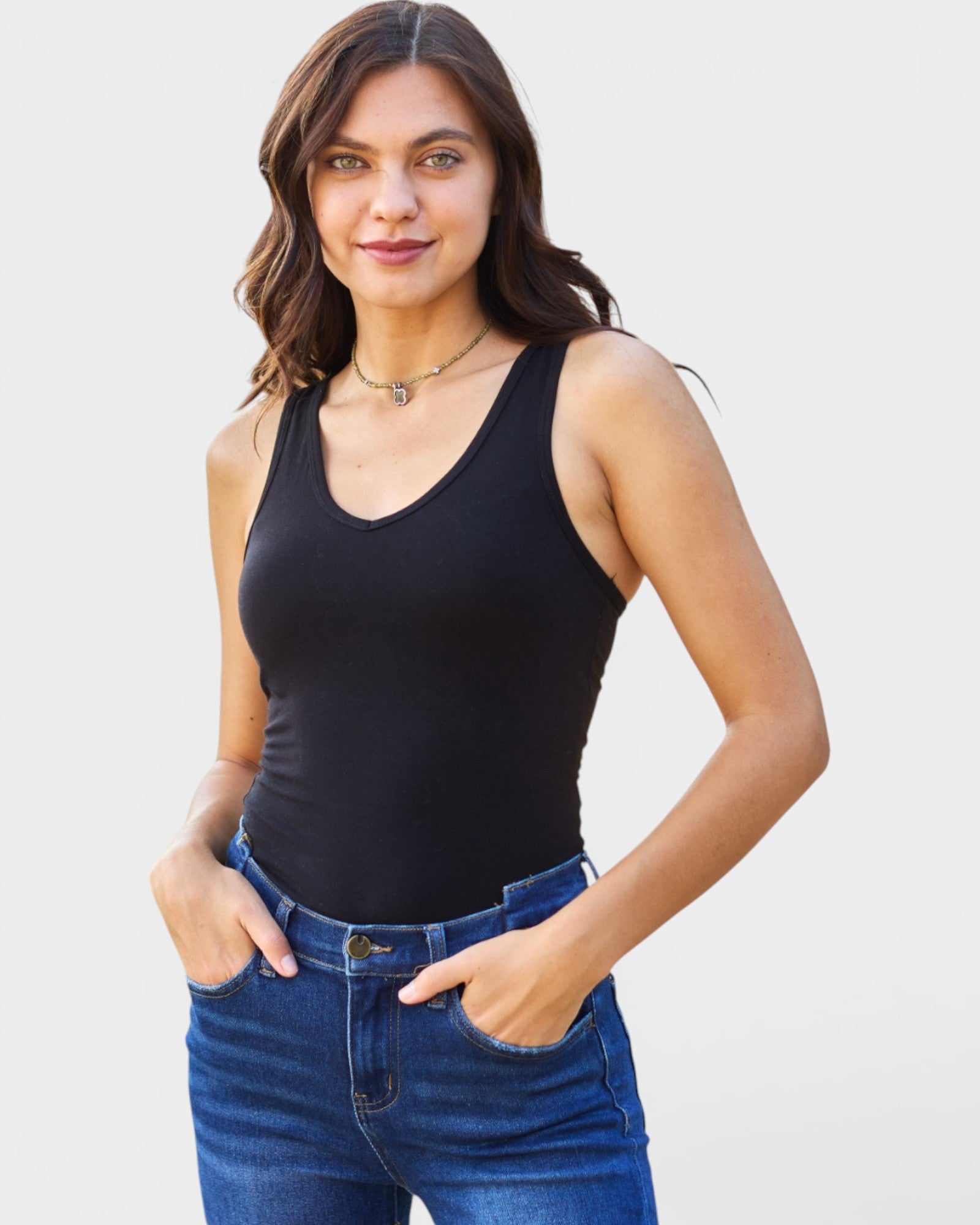 Woman wearing a black tank top and blue jeans against a light background