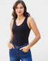 Woman wearing a black tank top and blue jeans against a light background