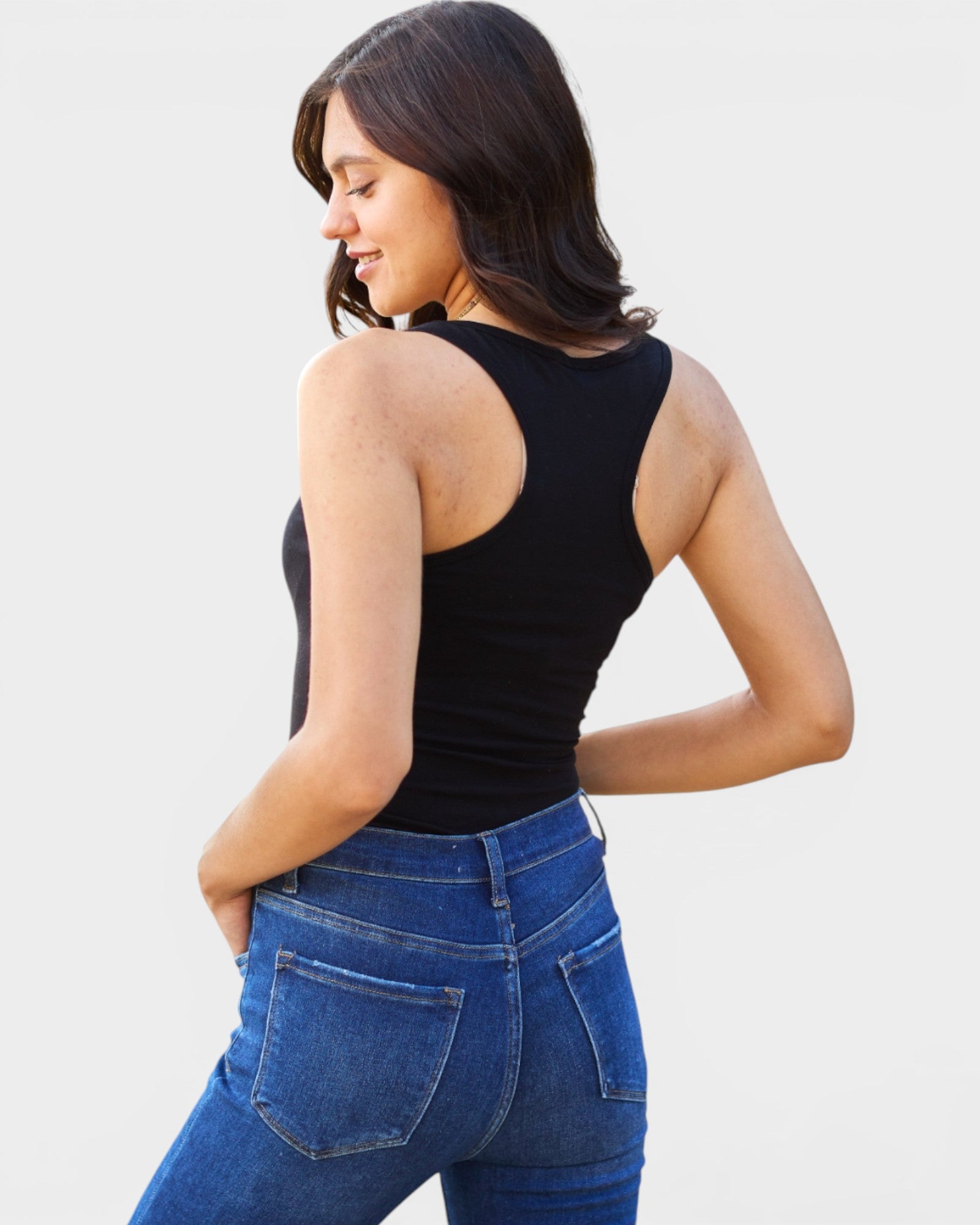 Woman wearing a black tank top and blue jeans on a light gray background
