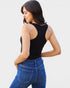 Woman wearing a black tank top and blue jeans on a light gray background