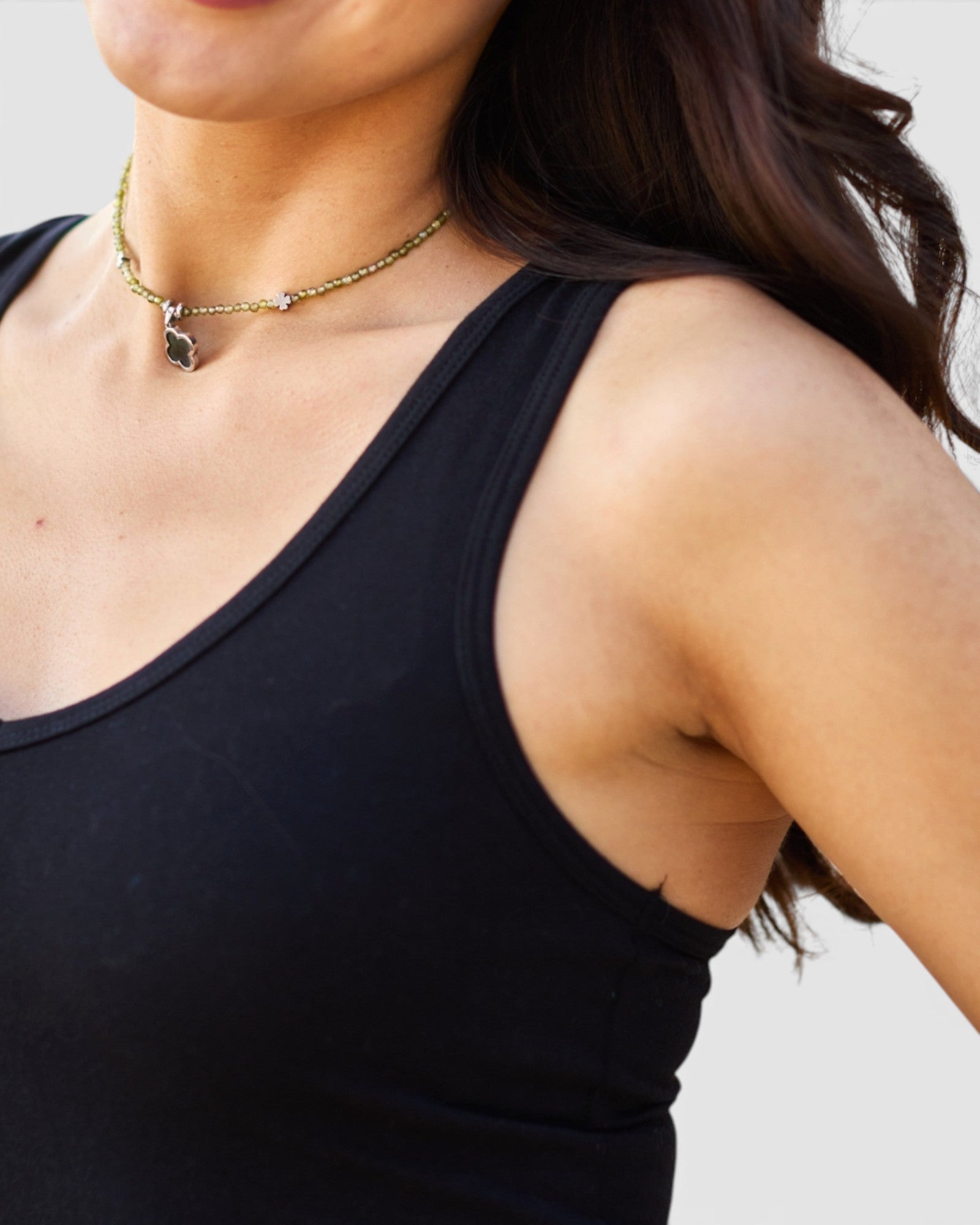 Woman wearing a black tank top and gold necklace against a neutral background