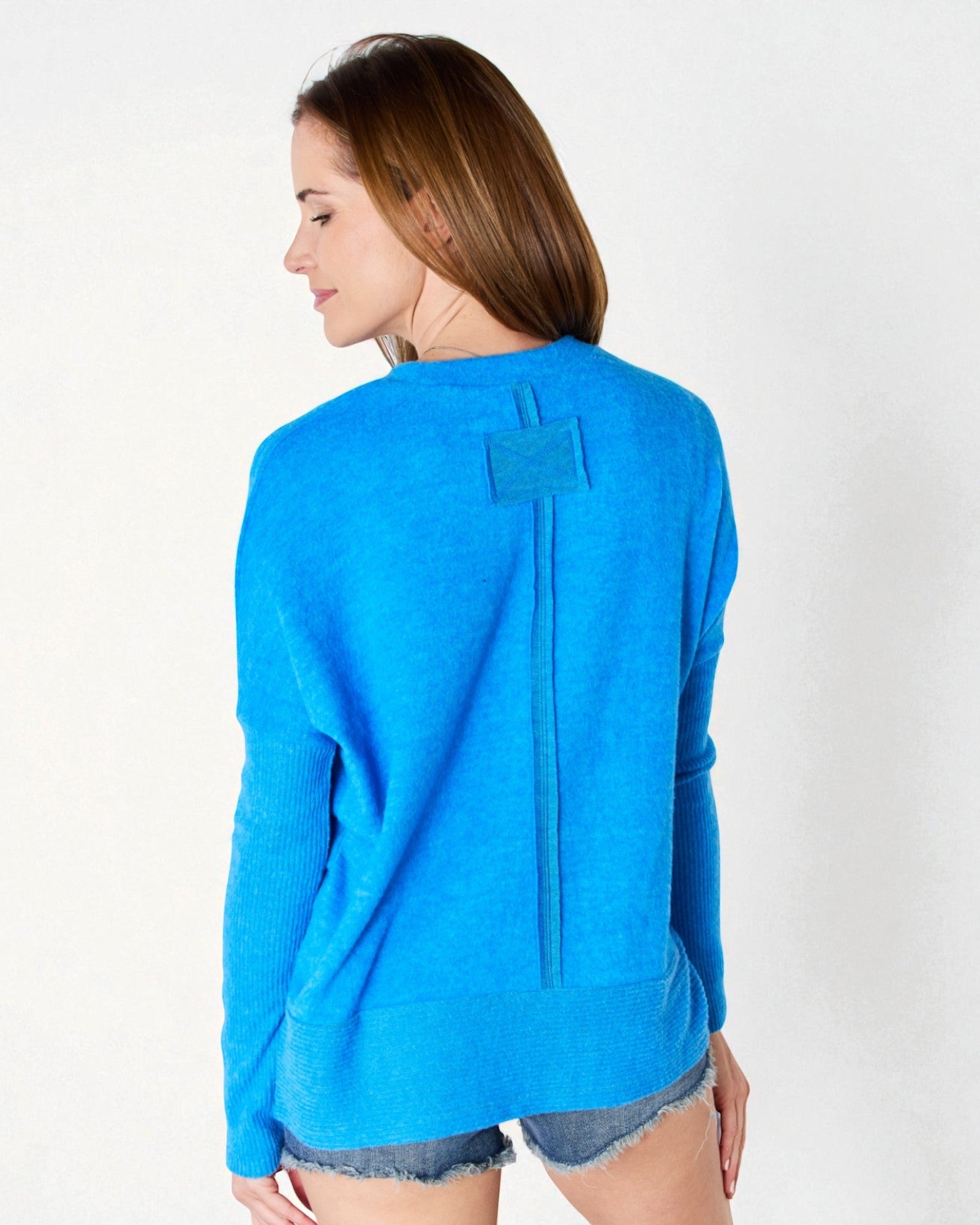 Woman wearing a blue sweater with a unique back design on a white background