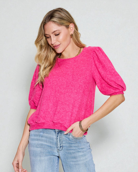 Woman wearing a bright pink top with puff sleeves against a plain background