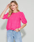 Woman wearing a bright pink top with puff sleeves and light blue jeans on a plain background