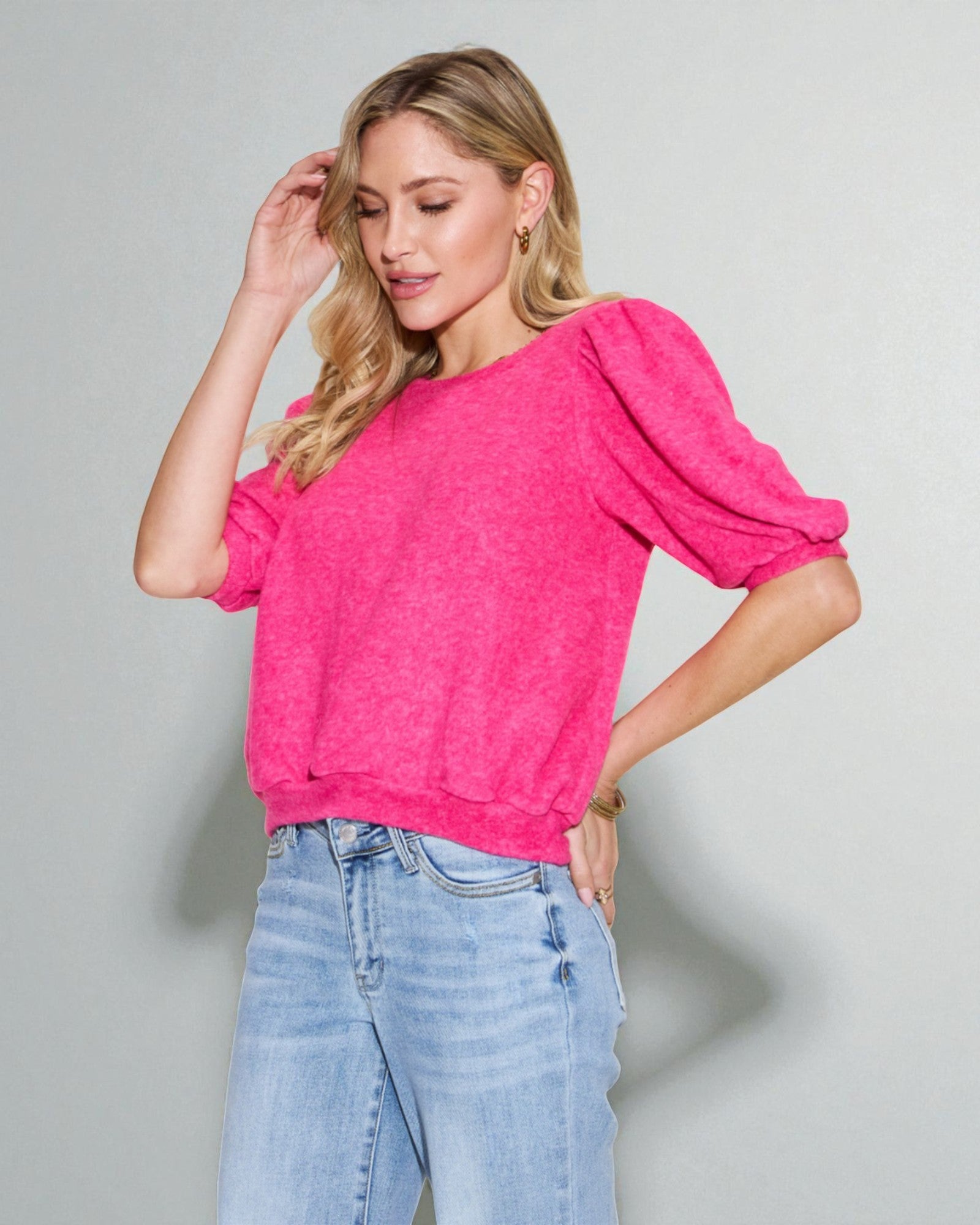 Woman wearing a bright pink top and light blue jeans against a plain background
