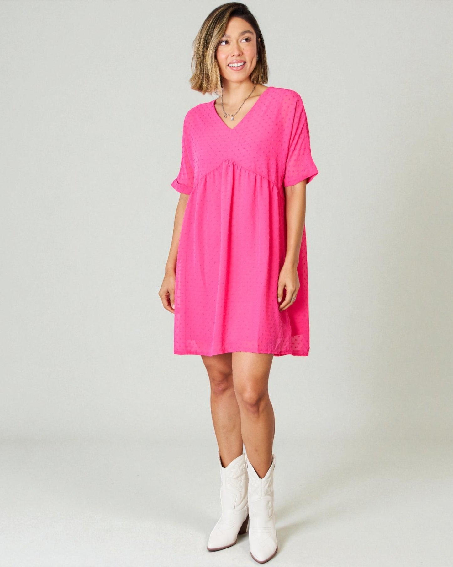 Woman wearing a bright pink dress with white boots on a plain background