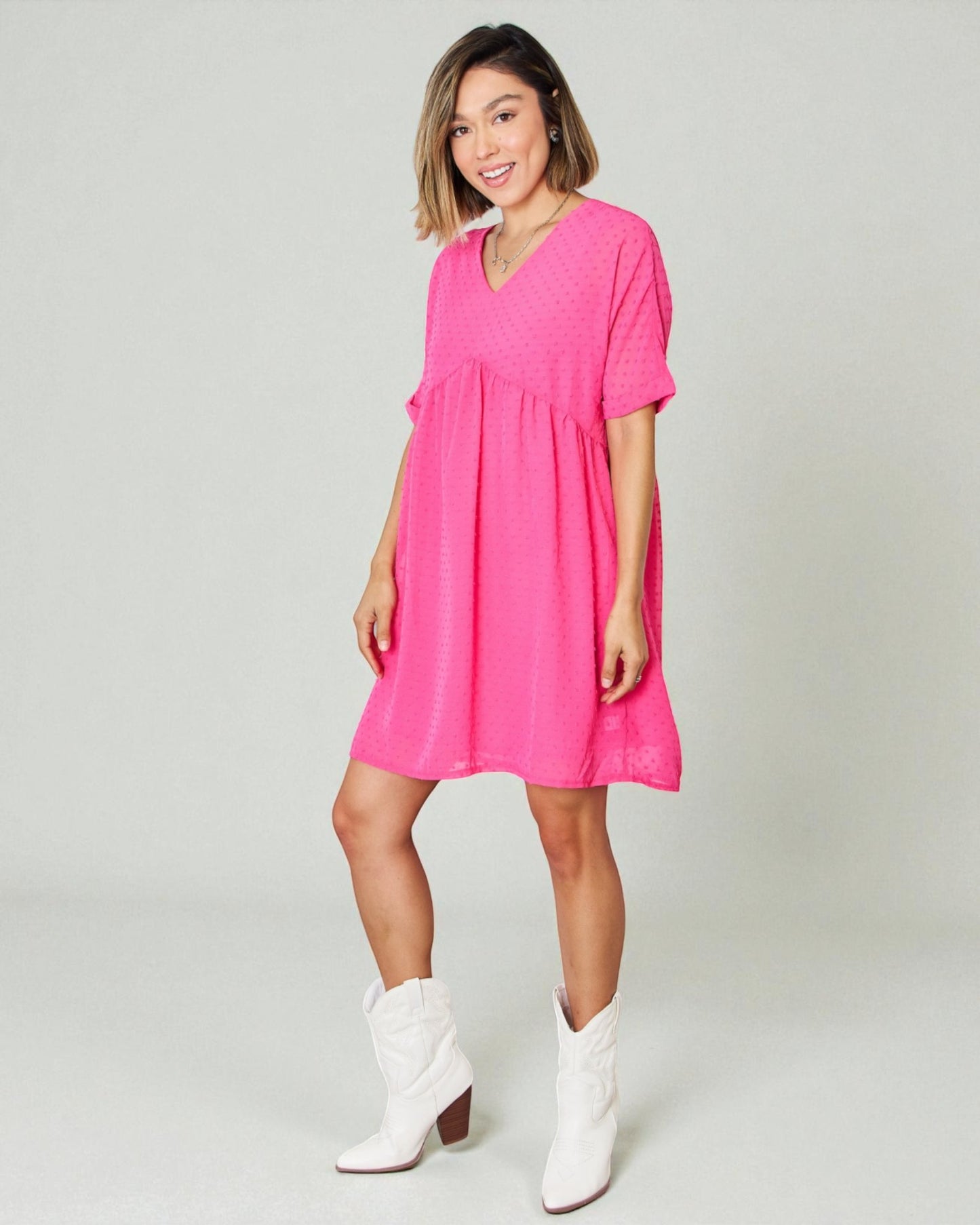 Woman wearing a bright pink dress and white boots on a plain background