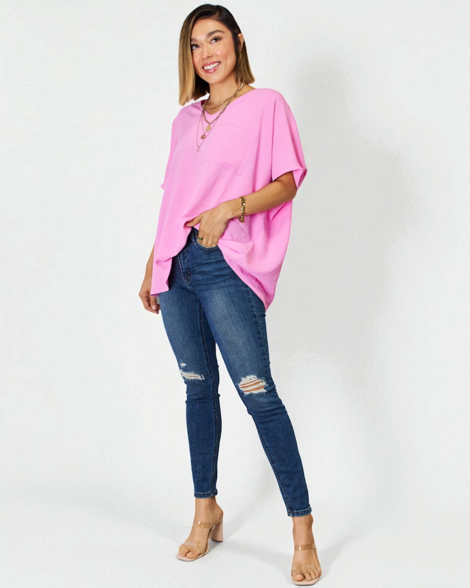 Woman wearing a pink oversized top and blue jeans on a white background