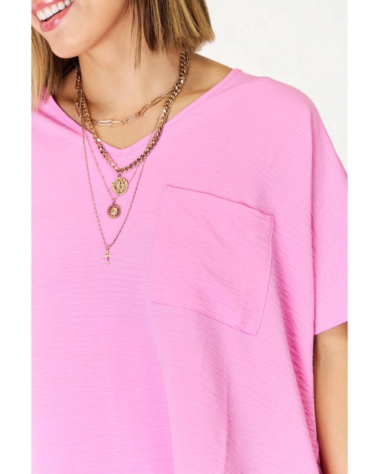 Person wearing a pink shirt with layered necklaces on a white background