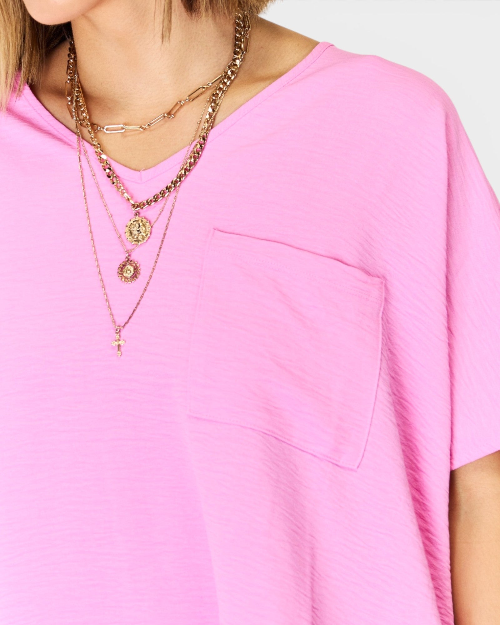 Person wearing a pink shirt with layered gold necklaces