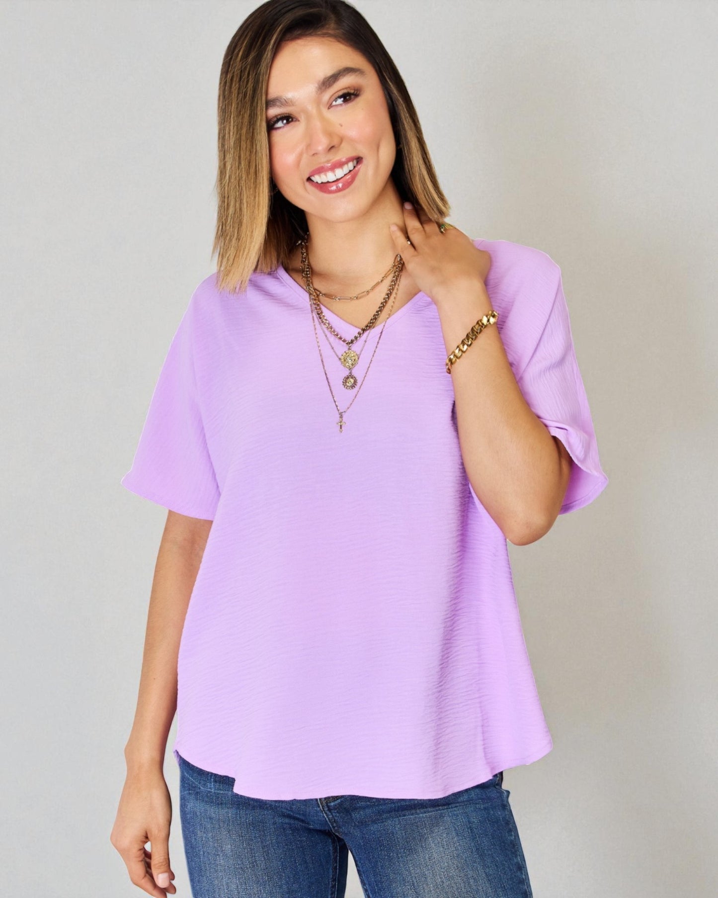 Woman wearing a light purple blouse and blue jeans against a plain background