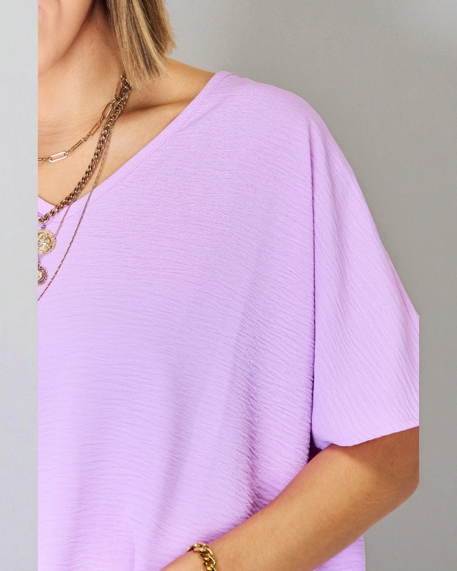 Person wearing a light purple top with gold jewelry on a gray background