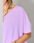 Person wearing a light purple top with gold jewelry on a gray background