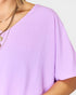 Close-up of a person wearing a light purple top with a plain background