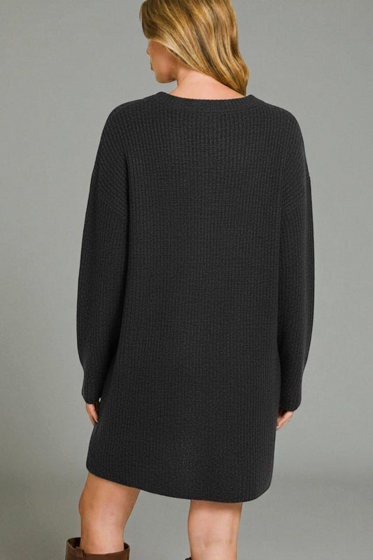 Person wearing a black sweater dress against a gray background