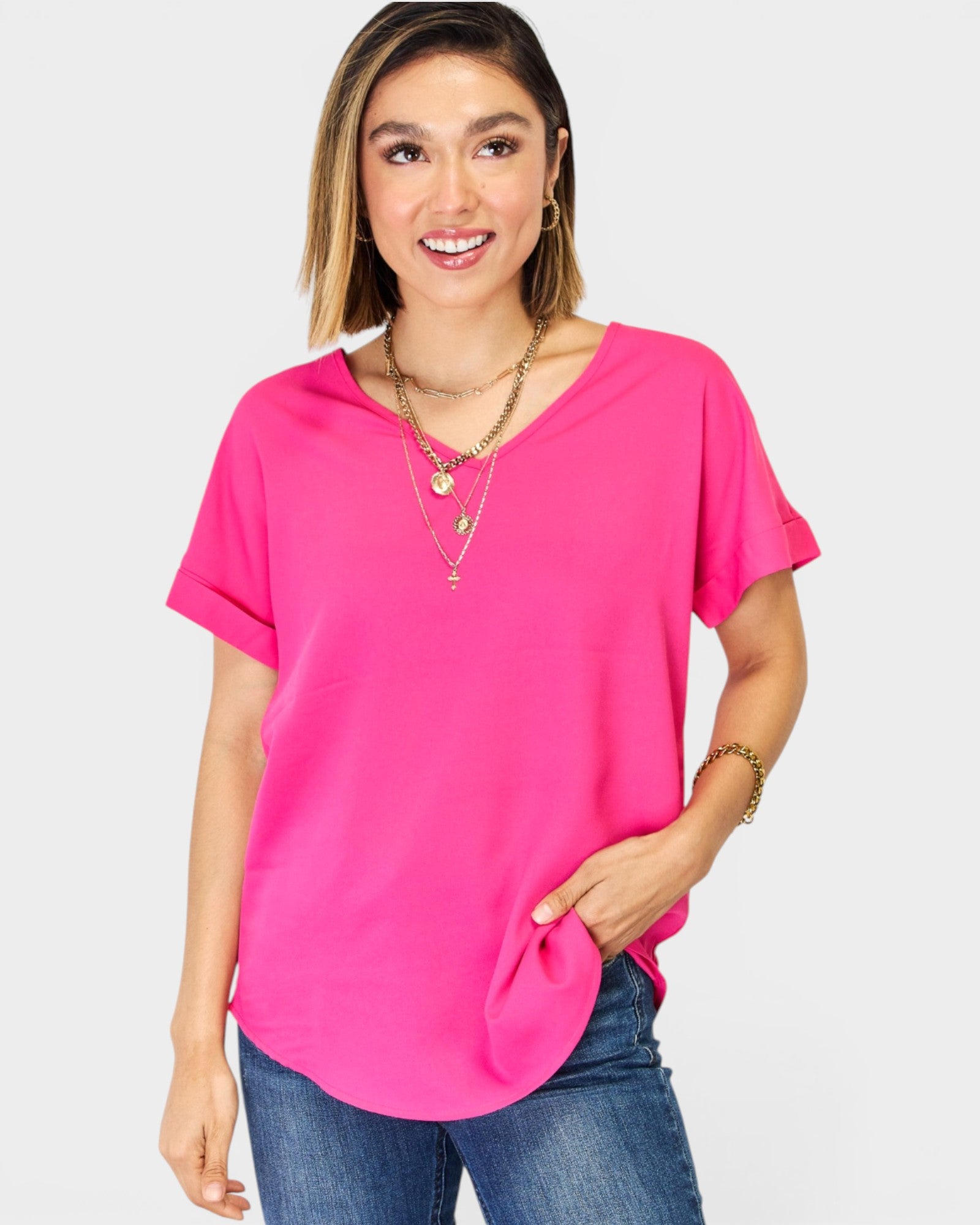 Woman wearing a bright pink top and blue jeans on a plain background