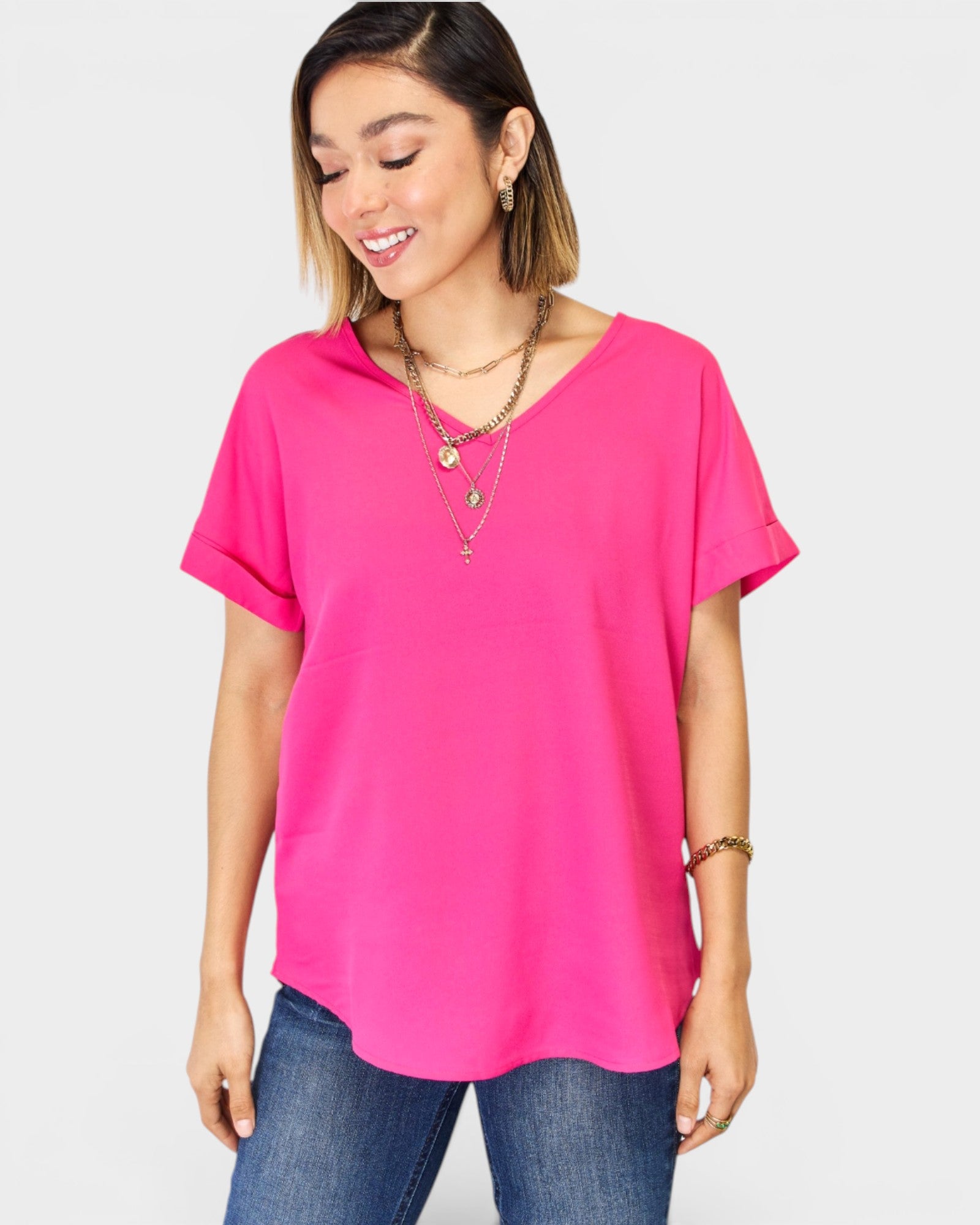 Woman wearing a bright pink top and blue jeans on a plain background