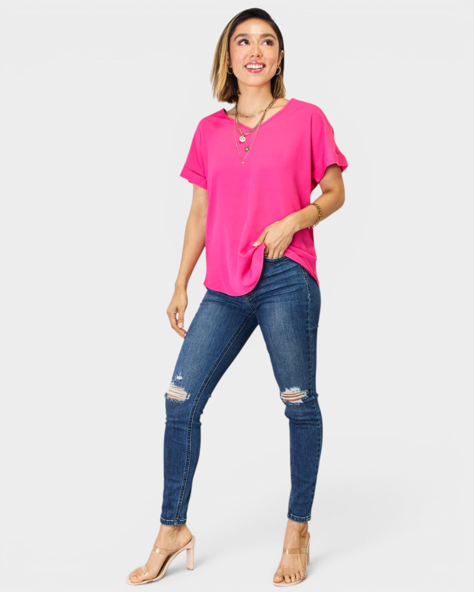 Woman wearing a bright pink top and blue jeans on a white background
