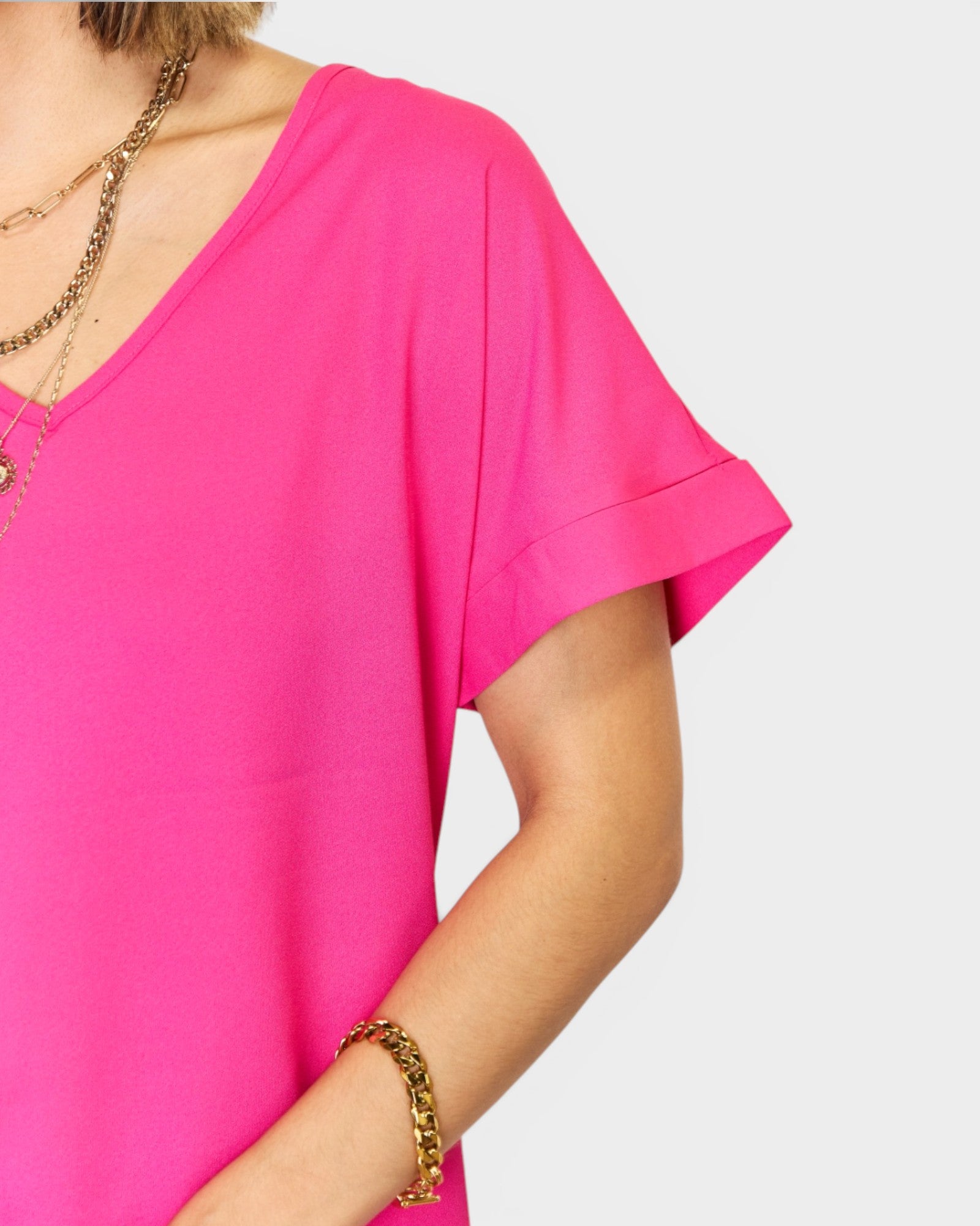 Person wearing a bright pink top with gold jewelry on a plain background