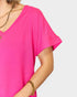 Person wearing a bright pink top with gold jewelry on a plain background