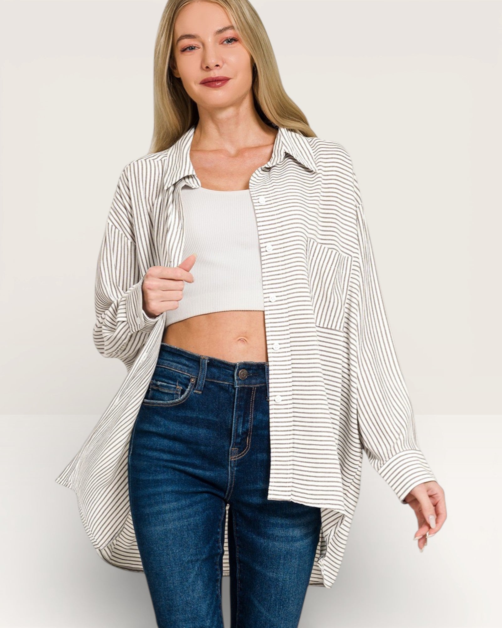 Woman wearing a striped shirt over a white top and blue jeans on a plain background