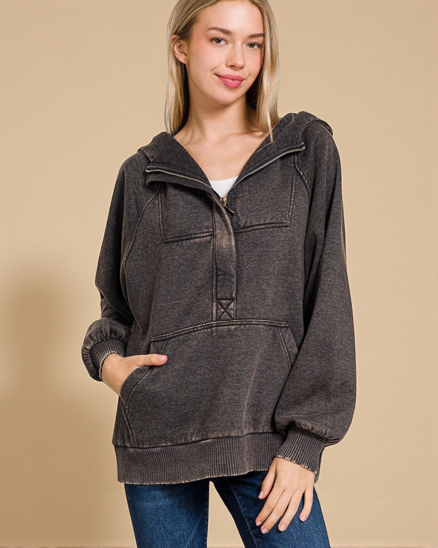 Woman wearing a dark gray hooded sweater against a beige background