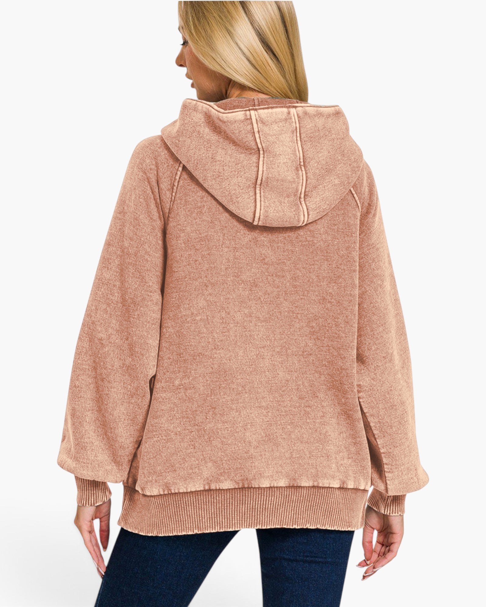 A woman shown from the back wearing a dusty rose hooded sweatshirt and dark blue jeans against a plain white studio background.