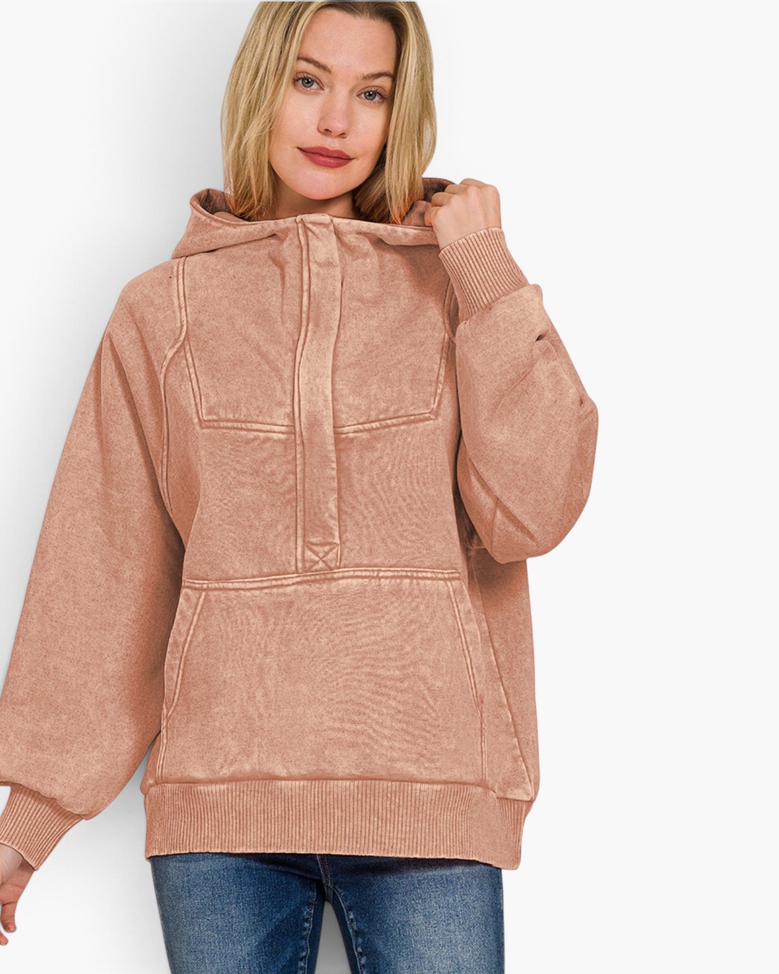 A woman wearing a dusty rose pink hooded sweatshirt with a unique textured fabric and ribbed cuffs, paired with blue jeans, against a plain white background.