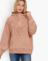 A woman wearing a dusty rose pink hooded sweatshirt with a unique textured fabric and ribbed cuffs, paired with blue jeans, against a plain white background.