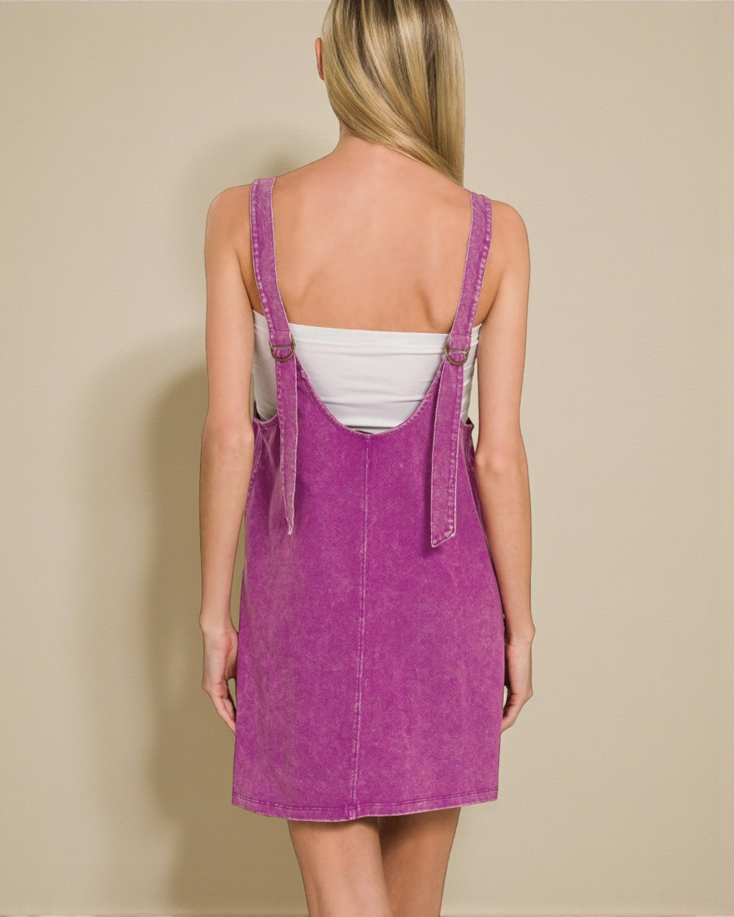 Person wearing a purple denim dress with a white top against a beige background