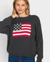 Person wearing a black sweater with an American flag design on a plain background