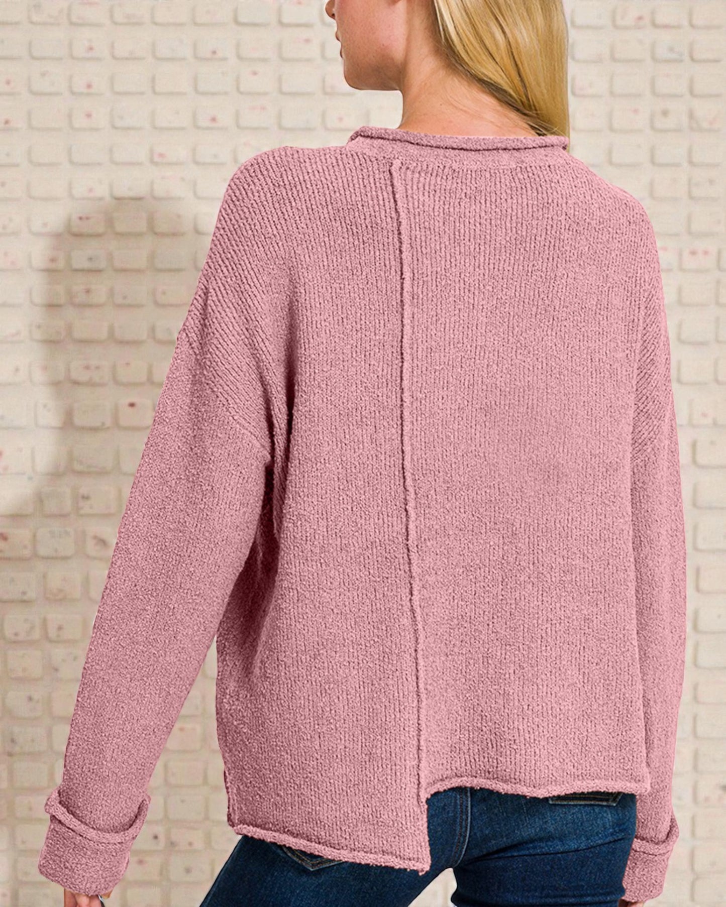 Pink cardigan worn by a person against a light brick wall.