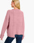 A woman shown from the back wearing a dusty pink ribbed knit sweater and blue jeans against a plain white background.