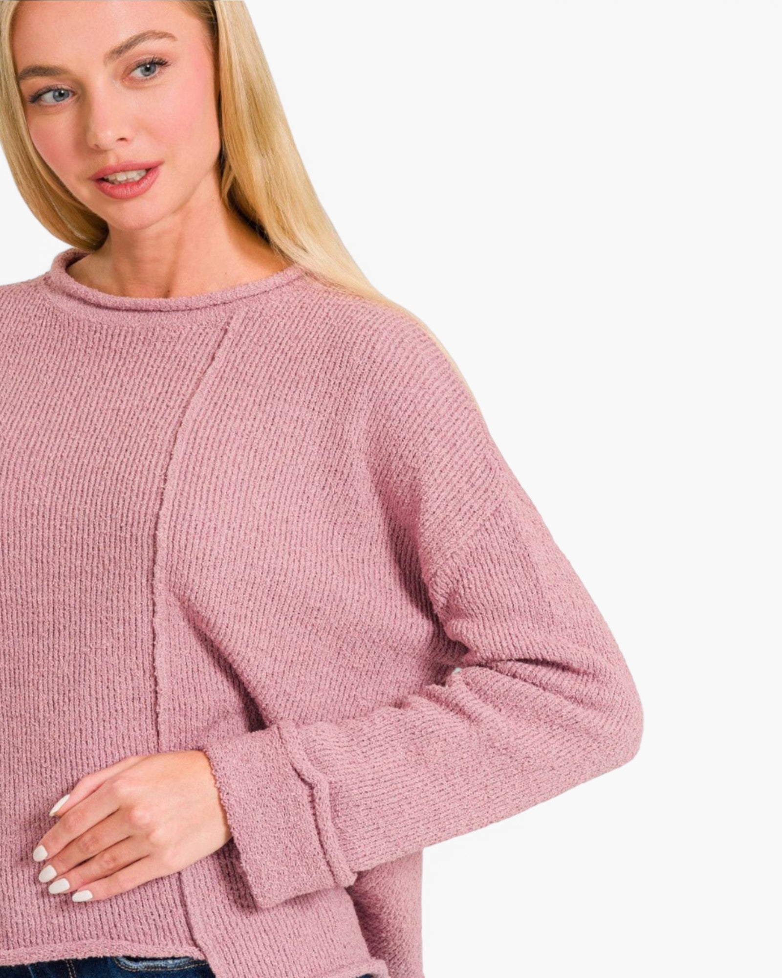A close-up of a woman wearing a dusty rose pink ribbed knit sweater against a plain white background.
