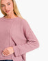 A close-up of a woman wearing a dusty rose pink ribbed knit sweater against a plain white background.